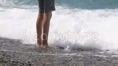 男孩`脚在海里，一个十几岁的少年站在海滩上的鹅卵石海滩上。 自然假期。